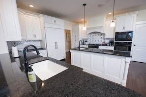 A modern kitchen with white cabinetry, a granite countertop, and stainless steel appliances. - Beautiful 4-Bedroom Modern Farmhouse located outside of Saint Joseph, IL (Saint Joseph)
