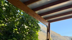 A covered outdoor seating area with a table, a lantern, and a view of a mountainous landscape. - Apartment 'Theodora' with Private Terrace, Wi-Fi and Air Conditioning (Panormos)