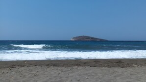 A beach with waves approaching the shore and a small island in the distance. - Apartment 'Theodora' with Private Terrace, Wi-Fi and Air Conditioning (Panormos)