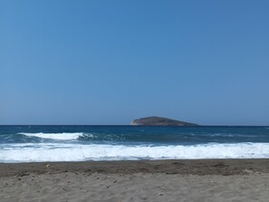 Ein Strand mit ankommenden Wellen und einer kleinen Insel in der Ferne.