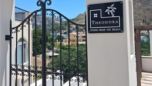 A gated entrance to a property named 'Theodora Studio Near the Beach' with a view of buildings and greenery in the background. - Apartment 'Theodora' with Private Terrace, Wi-Fi and Air Conditioning (Panormos)