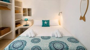 A hotel room with a bed, a nightstand, a lamp, a wardrobe, and a wall decoration. - Apartment 'Theodora' with Private Terrace, Wi-Fi and Air Conditioning (Panormos)