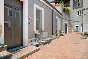 Un edificio con fachada gris, una puerta y ventanas. Cuenta con un pequeño espacio exterior con una mesa y sillas.