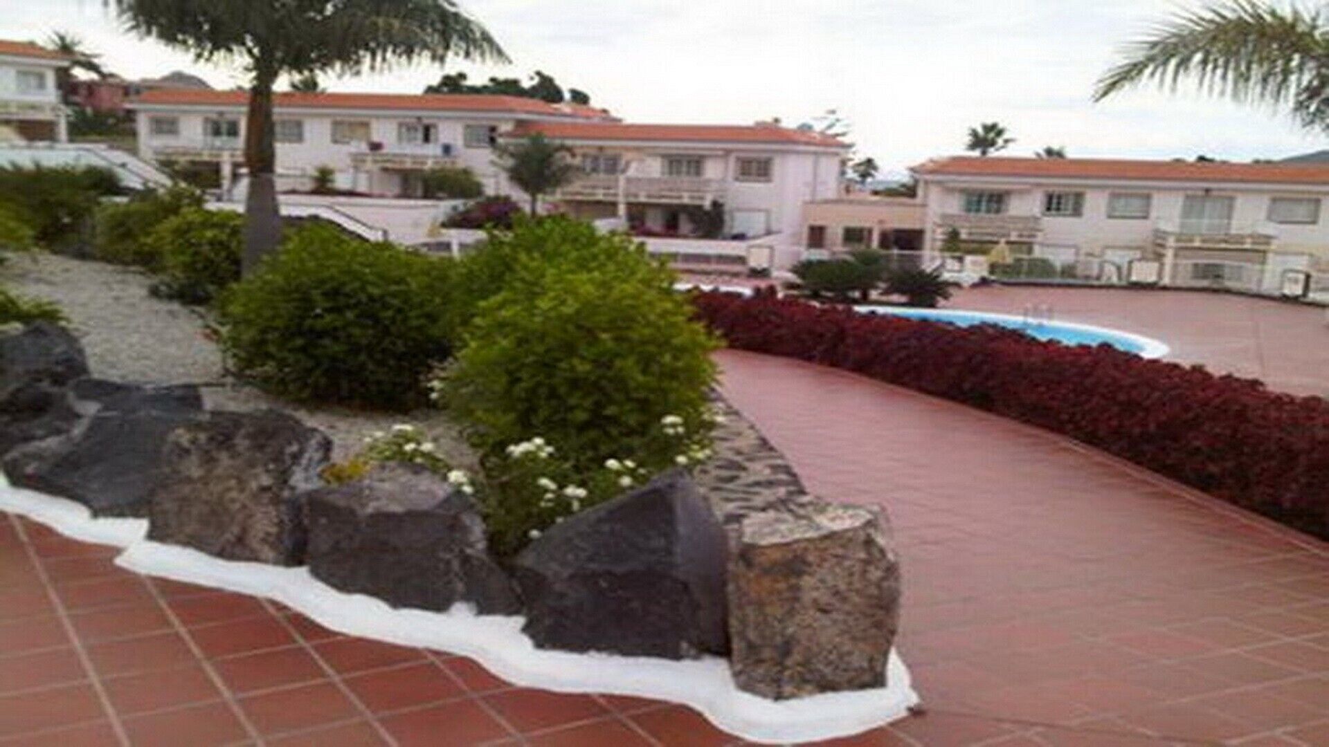 Un barrio residencial con un sendero pavimentado, una piscina y casas con tejados de tejas rojas.