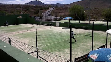 An outdoor tennis court with a net, surrounded by a fence, and a road in the background.