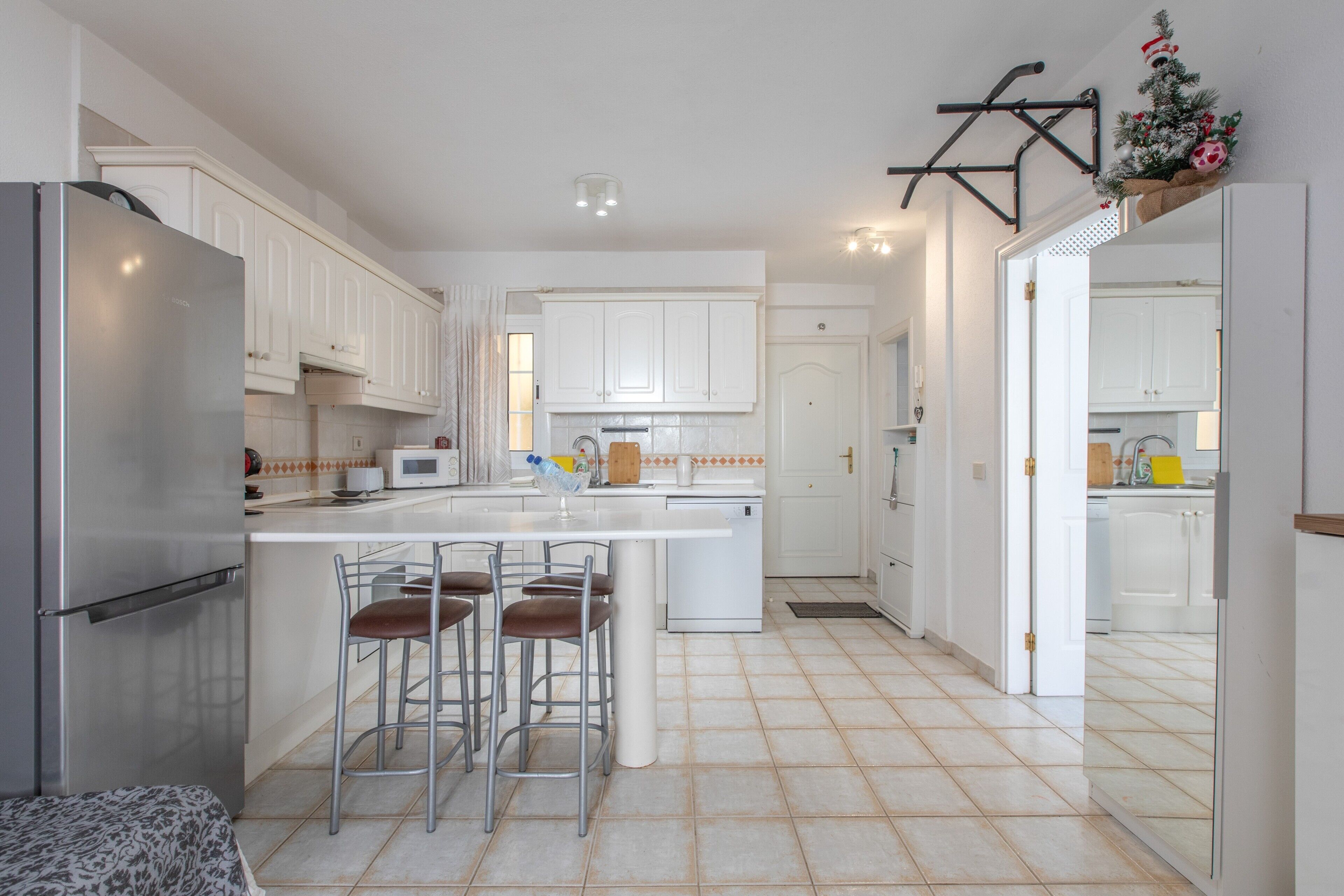 Una cocina moderna con gabinetes blancos, una isla central con taburetes de bar y un refrigerador de acero inoxidable.