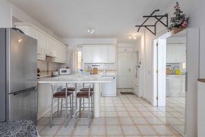 Una cocina moderna con gabinetes blancos, una isla central con taburetes de bar y un refrigerador de acero inoxidable.