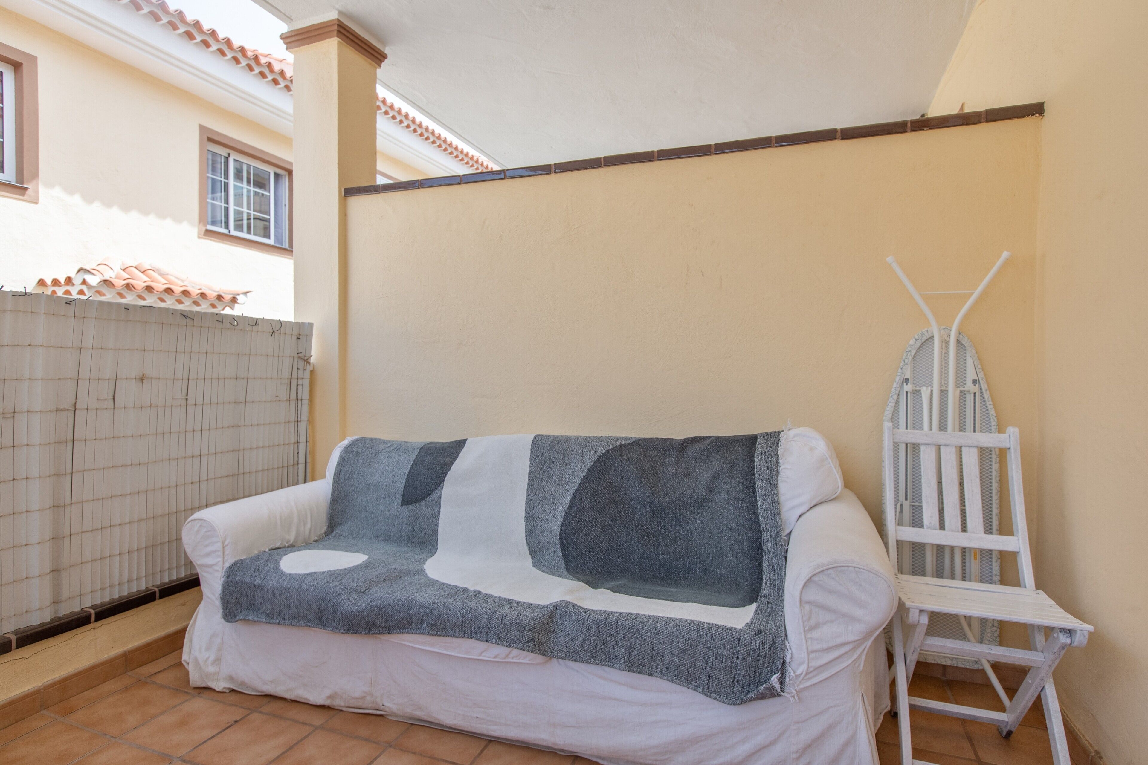 Un espace extérieur aménagé avec des sièges blancs, comprenant un canapé couvert et une chaise en métal blanche.