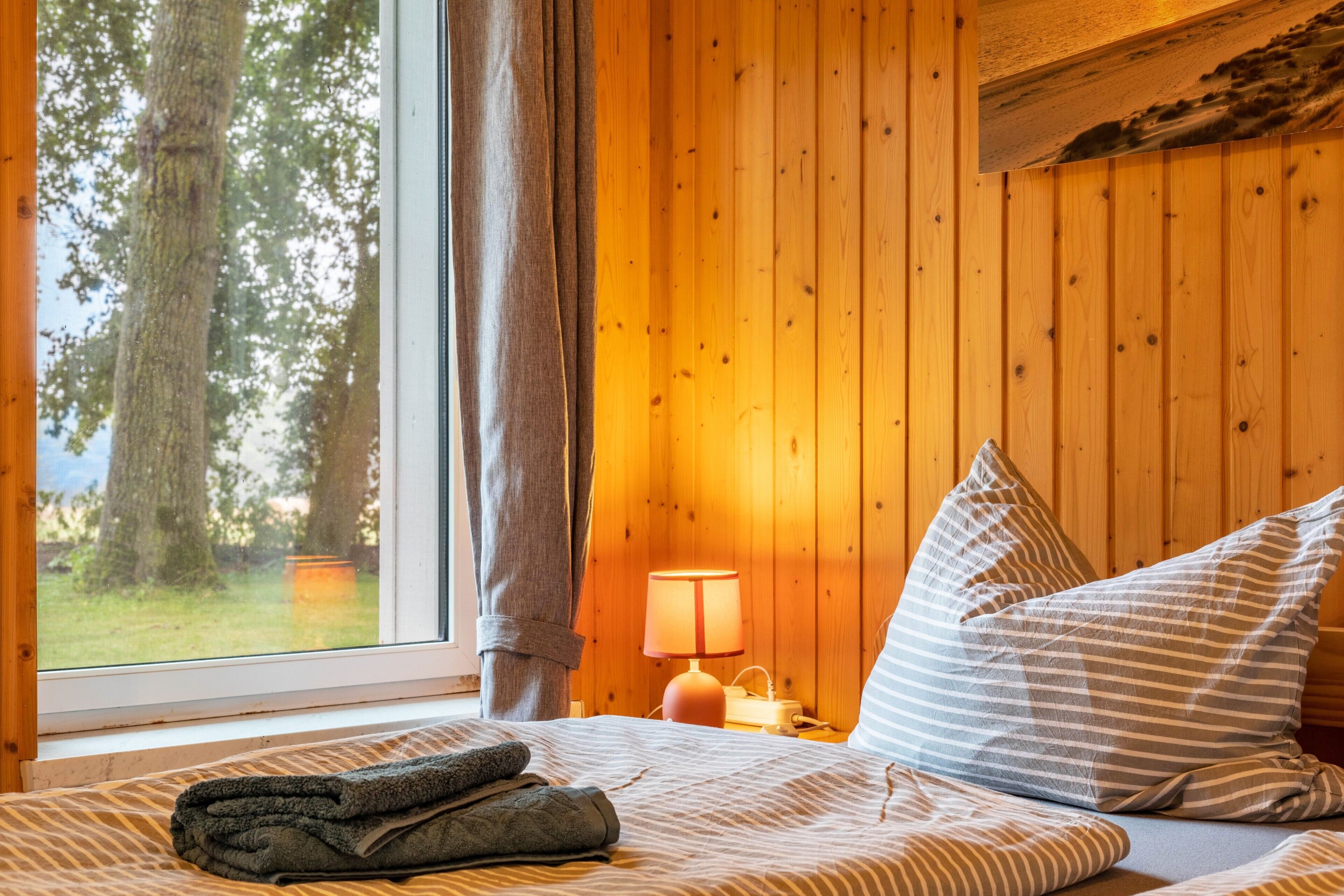 Ein Schlafzimmer mit einem Bett, Kissen, einer Lampe und einem Fenster mit Vorhängen.