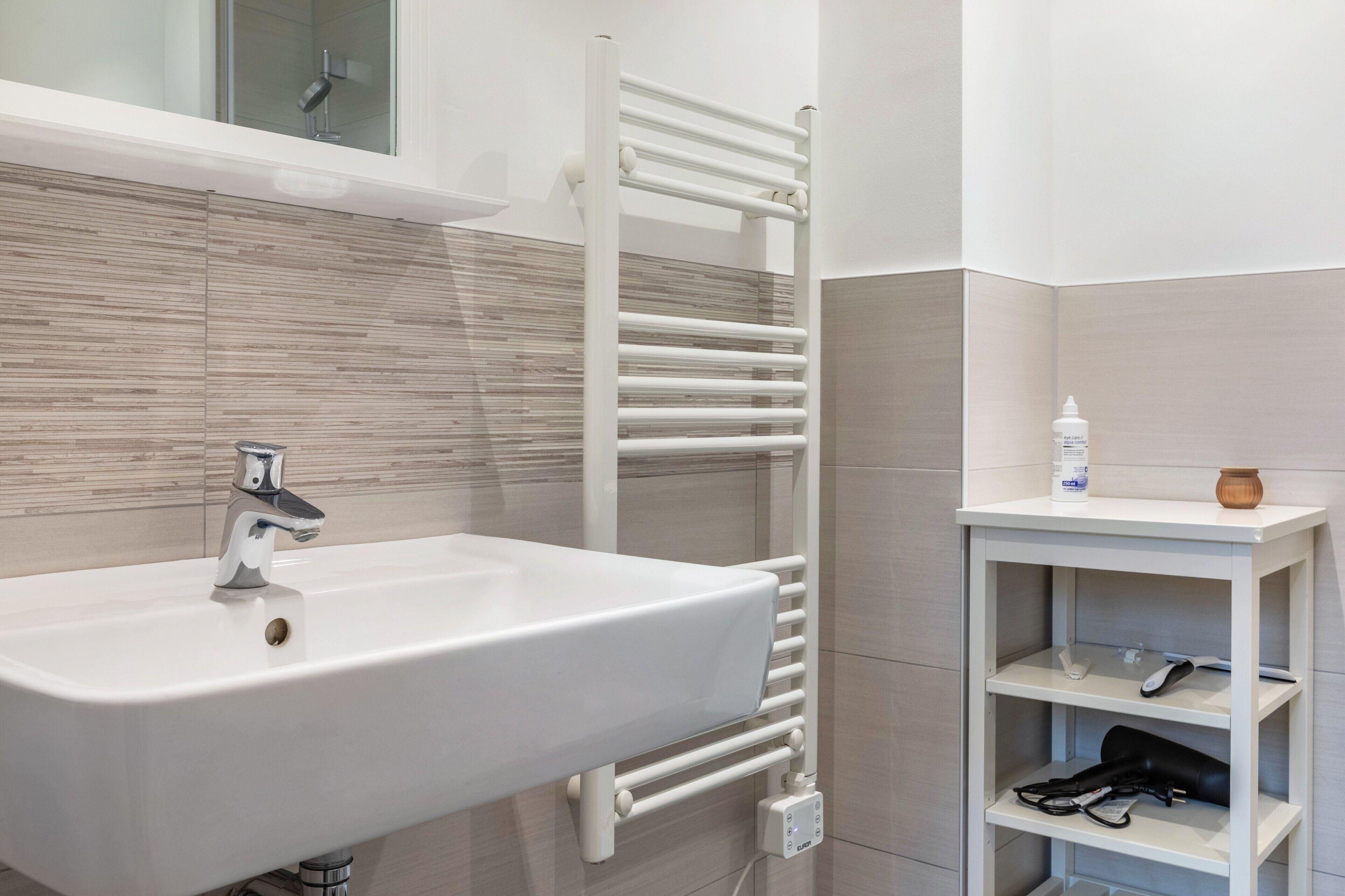Un baño moderno con un lavamanos blanco, un perchero y un estante con artículos de aseo.