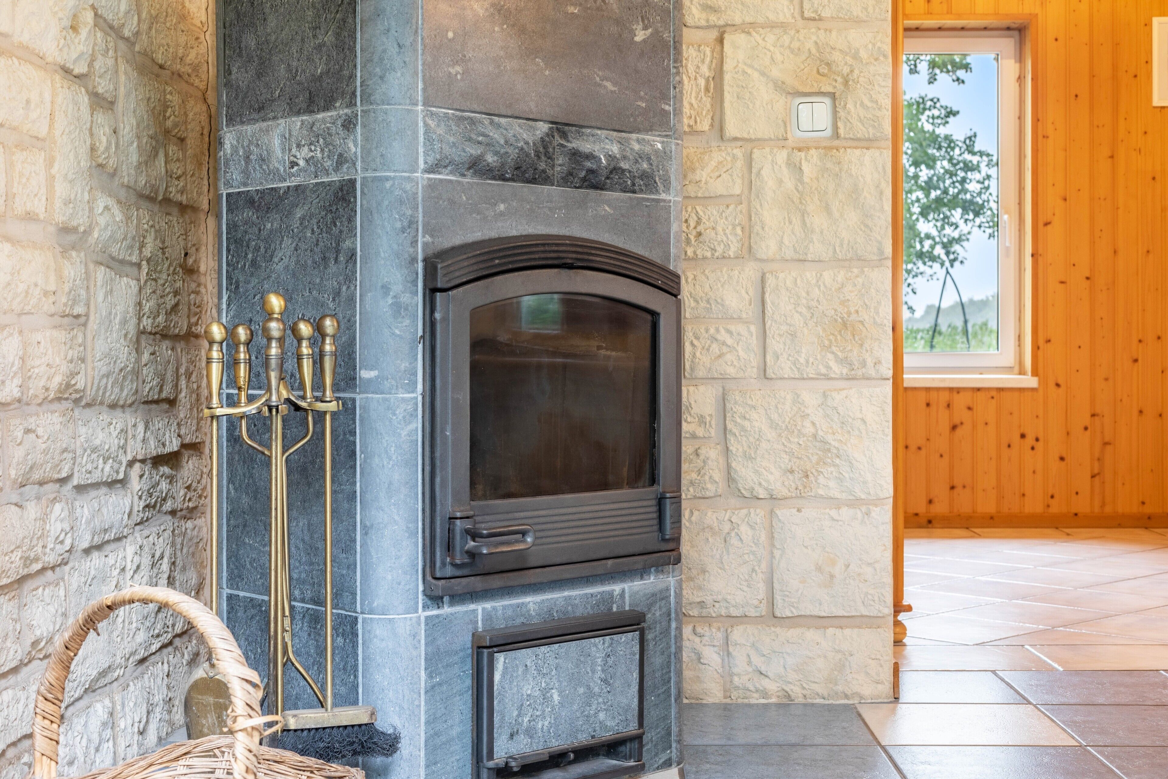 A stone fireplace with a glass door, a candelabra, and a wicker basket.