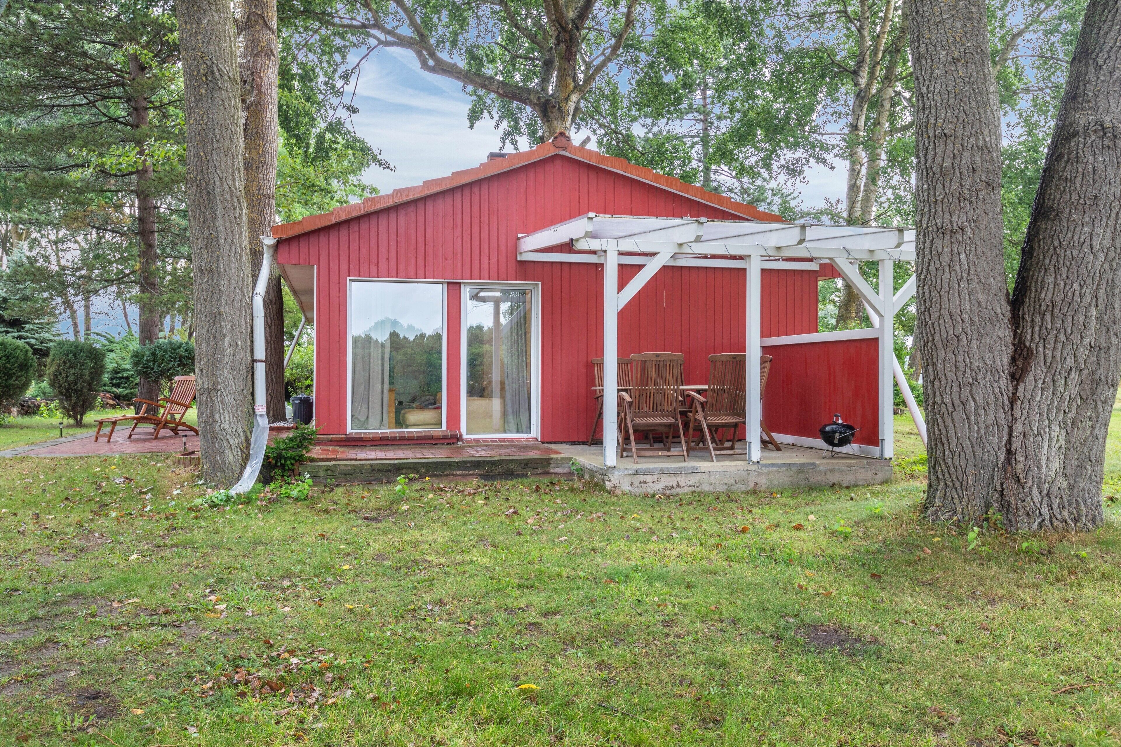 Une cabane en bois rouge avec un patio couvert et un barbecue.