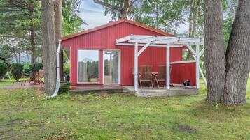Une cabane en bois rouge avec un patio couvert et un barbecue.