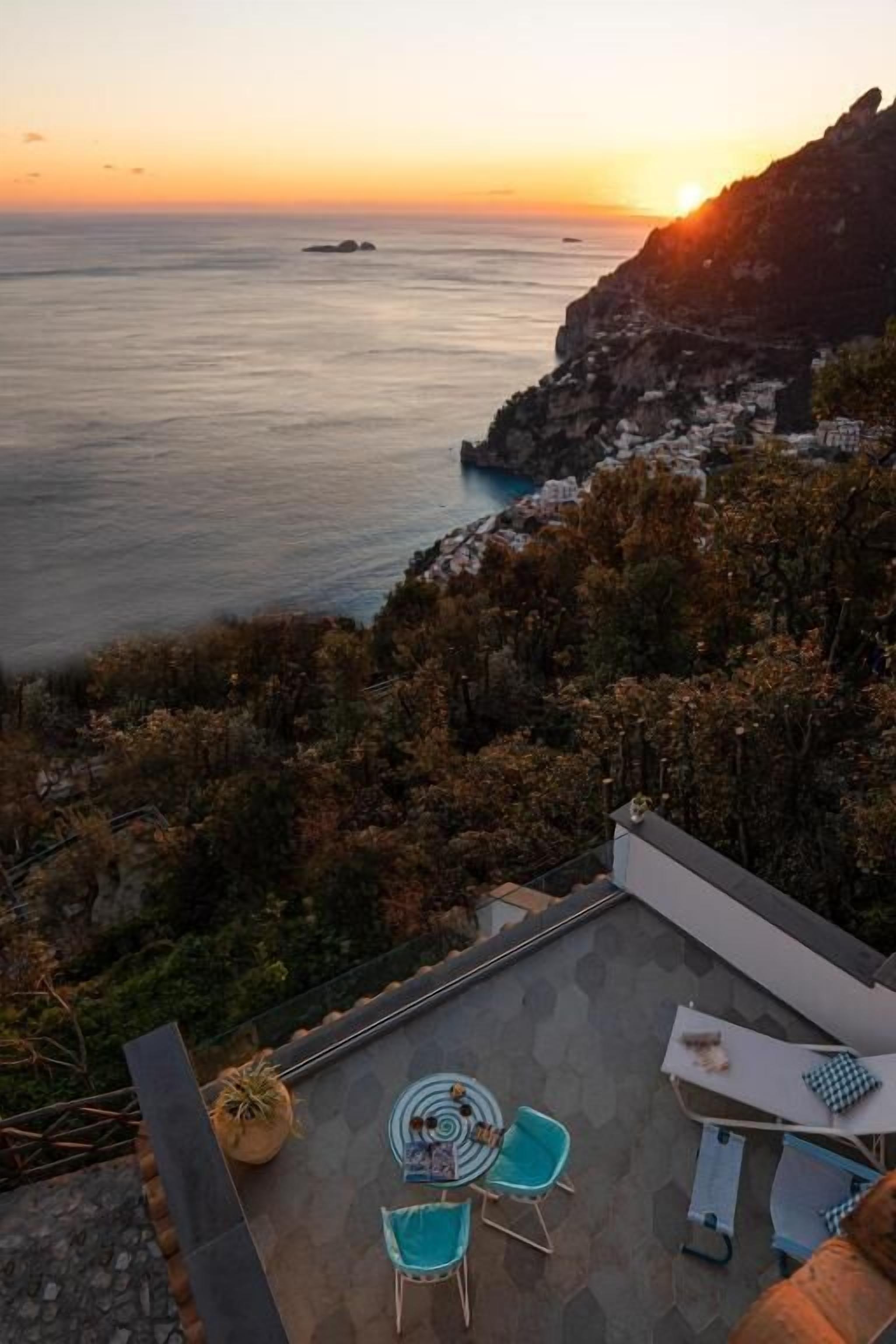 A terrace with a table and chairs, overlooking a coastal landscape with cliffs and the sea.