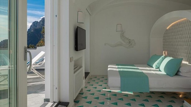 A bedroom with a bed, a TV, and a view of mountains. - Petrea Lifestyle Suites (Positano)