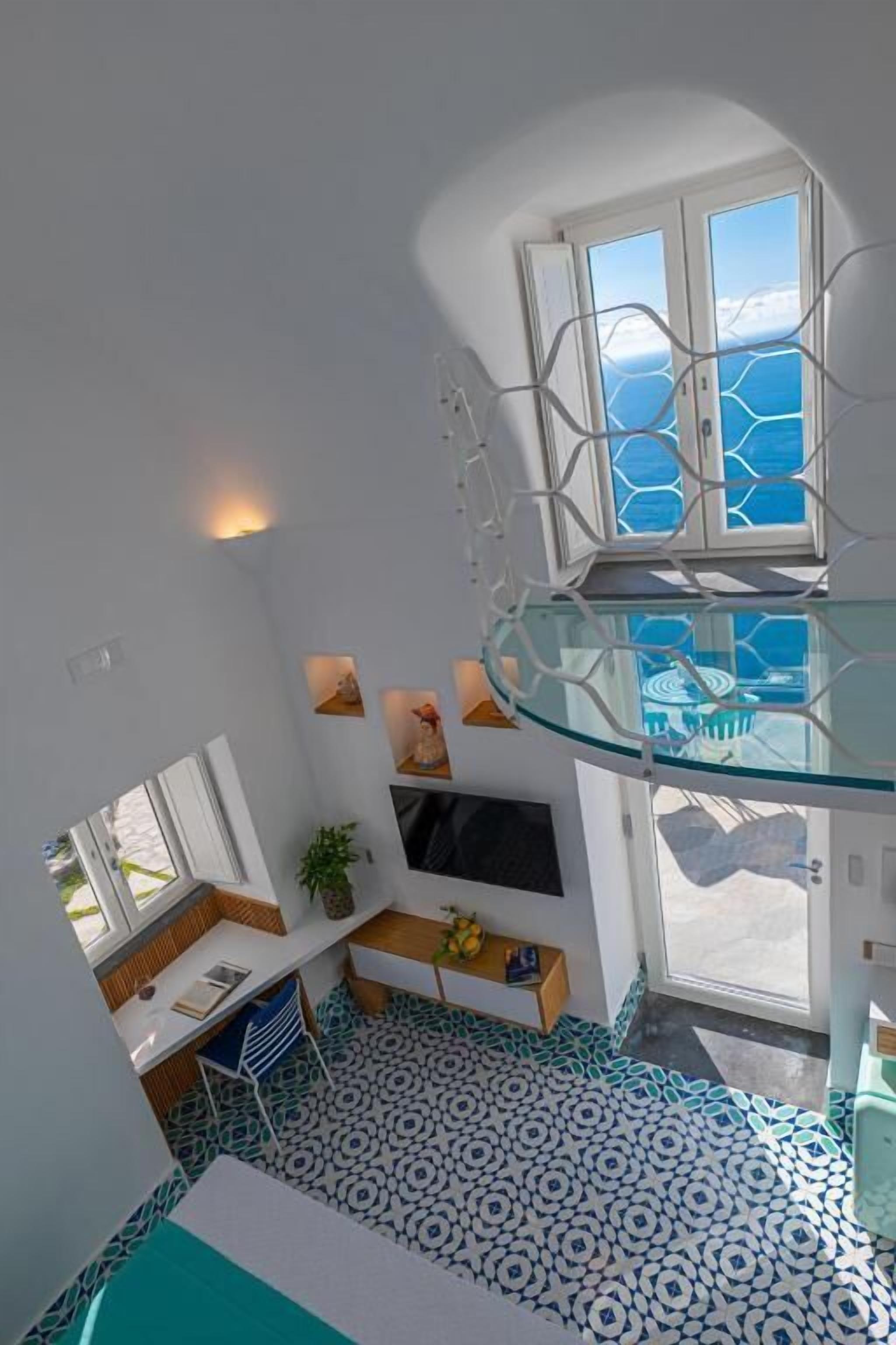 A room with a curved glass balcony, a flat-screen TV, a small seating area, and a patterned floor.