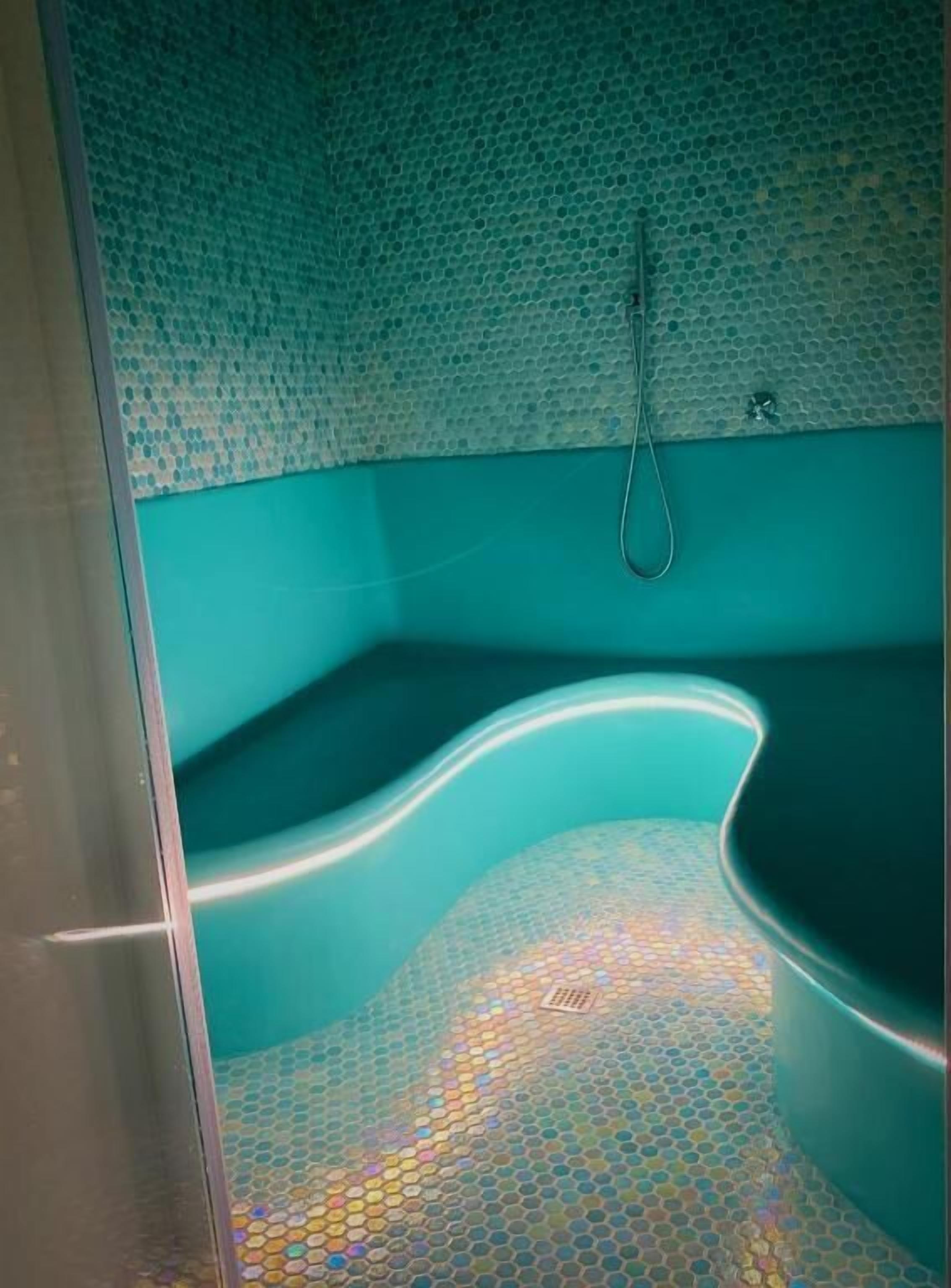 Une salle de bain avec une baignoire à bords arrondis, un espace douche et un sol carrelé.