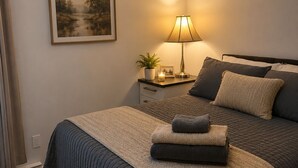 A bedroom with a bed, bedside table, lamp, and a framed picture on the wall. - 	
Quiet Executive Retreat | Balcony, Parking, Near Hospital & UdeM” (Moncton)