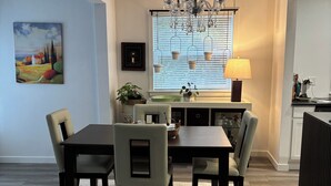 A dining area with a table and chairs, a chandelier, a window with blinds, and a painting on the wall. - 	
Quiet Executive Retreat | Balcony, Parking, Near Hospital & UdeM” (Moncton)