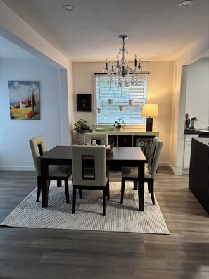 A dining area with a table and chairs, a chandelier, a window with blinds, and a painting on the wall. - 	
Quiet Executive Retreat | Balcony, Parking, Near Hospital & UdeM” (Moncton)