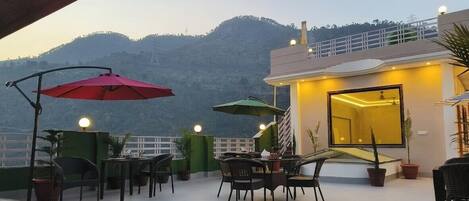 A rooftop terrace with outdoor seating, a view of a mountain, and a building with a balcony.