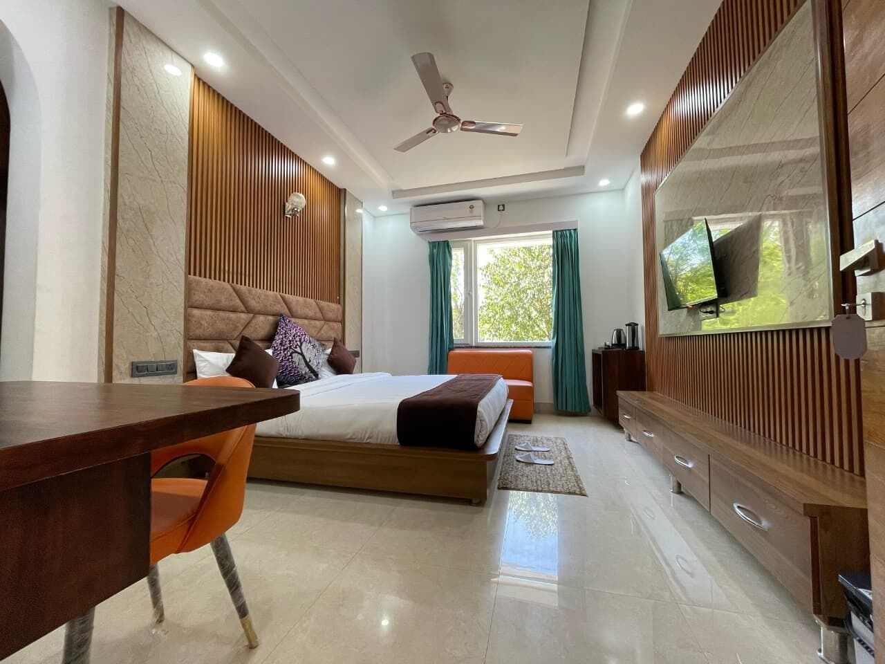 A modern hotel room with a bed, a desk, a TV, and a ceiling fan.