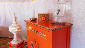 Une pièce avec un plancher en bois, un buffet rouge orné de motifs décoratifs, une lampe blanche et un distributeur d’eau.