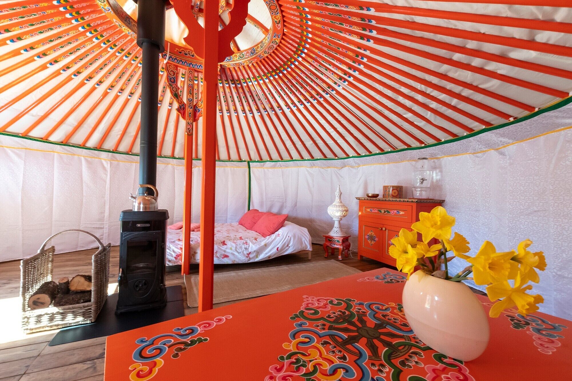 A room with a bed, a table with a vase, a heater, and a water dispenser.