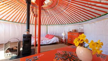 A room with a bed, a table with a vase, a heater, and a water dispenser.