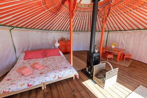 Una habitación acogedora con cama, mesa, silla, cesta y estufa de leña.