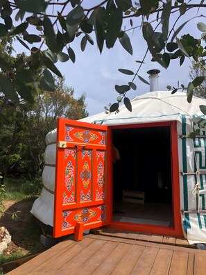 A traditional yurt with an open entrance, a wooden deck, and a chimney.