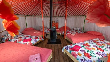 Une chambre avec quatre lits, chacun recouvert d’une couvre-lit à motifs floraux et agrémenté d’un oreiller rose. On y trouve une table en bois placée au centre et un radiateur noir.
