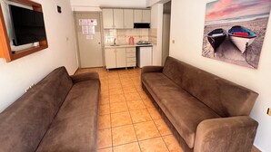 Ein Wohnzimmer mit zwei Sofas, einer Küche im Hintergrund und einem Gemälde von Booten an der Wand.