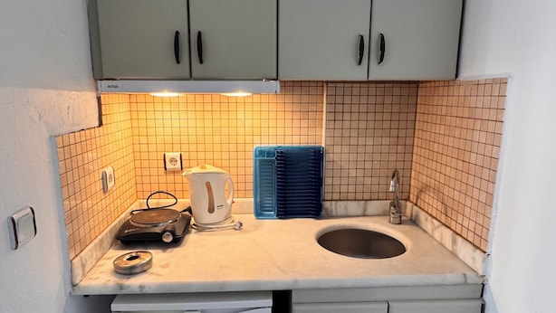 Eine kompakte Küche mit weißen Schränken, einer Spüle, einem kleinen Kühlschrank und einer gefliesten Rückwand.