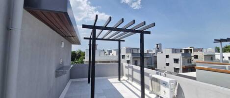Eine Dachterrasse mit einer Pergola, Klimaanlagen und Blick auf die umliegenden Gebäude.