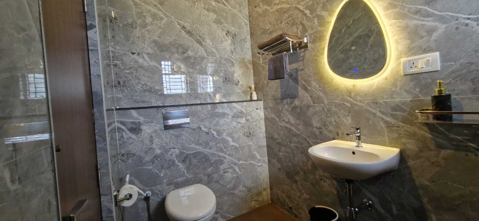 A bathroom with a marble wall, a glass shower enclosure, a toilet, a sink with a mirror, and a towel rack.