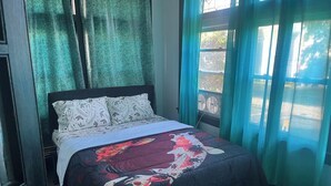 A bed with floral bedding, a dark headboard, and a window with curtains.