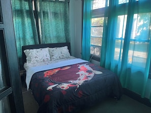 Una cama con ropa de cama floral, cabecera oscura y ventana con cortinas.