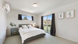 A bedroom with a bed, bedside tables, a potted plant, and a view through a large window. - Walk to Light Rail, Stylish Retreat w/Parking + AC (Seattle)
