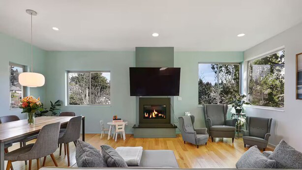 A modern living room with a fireplace, seating area, and a dining table. - Walk to Light Rail, Stylish Retreat w/Parking + AC (Seattle)