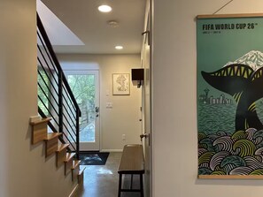 A hallway with a staircase, a door, and a poster of the FIFA World Cup 26. - Walk to Light Rail, Stylish Retreat w/Parking + AC (Seattle)