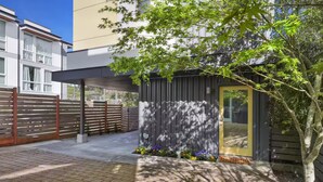 A modern building with a covered entrance, a gated area, and a small garden with flowers. - Walk to Light Rail, Stylish Retreat w/Parking + AC (Seattle)