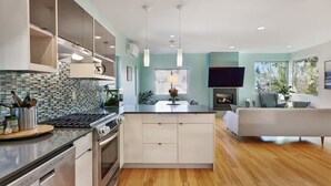 A modern kitchen with a central island, built-in appliances, and a dining area with a flat-screen TV and fireplace. - Walk to Light Rail, Stylish Retreat w/Parking + AC (Seattle)