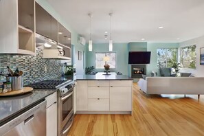 A modern kitchen with a central island, built-in appliances, and a dining area with a flat-screen TV and fireplace. - Walk to Light Rail, Stylish Retreat w/Parking + AC (Seattle)