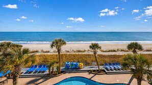 A pool area with lounge chairs and a view of the beach.