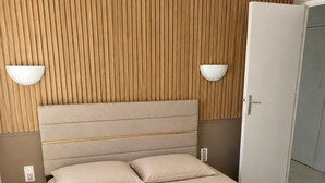 Uma cama com cabeceira, duas luminárias de cabeceira e um painel ripado de madeira ao fundo.