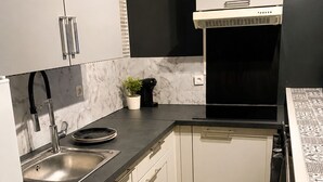 Uma cozinha compacta com armários brancos, bancada preta, pia de aço inoxidável e exaustor preto.