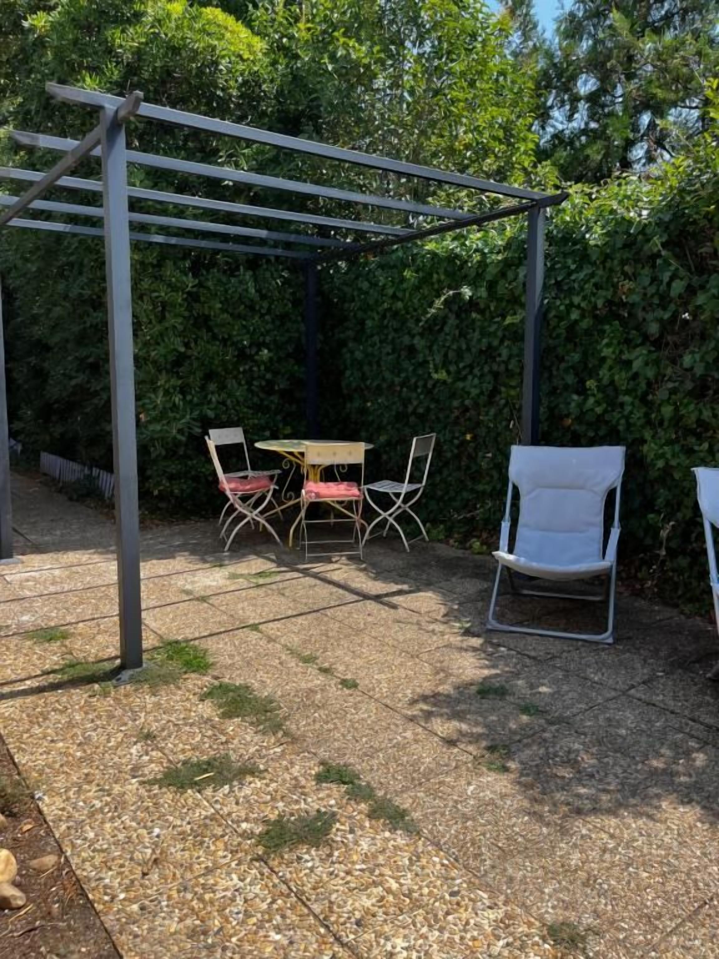 Un espacio de patio al aire libre con una pérgola, una mesa y cuatro sillas.