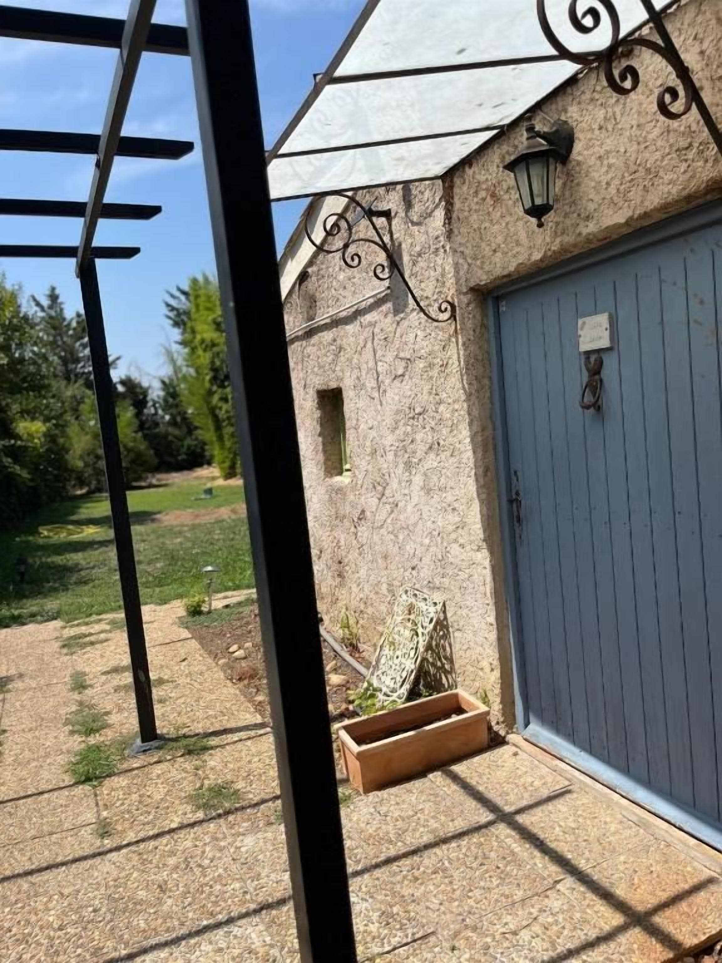 Un edificio con una puerta de garaje azul, un ventanal pequeño y un aplique de pared.