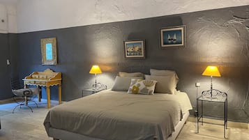 Une chambre à coucher avec un lit, deux tables de chevet avec des lampes, une chaise, une petite table et deux tableaux encadrés accrochés au mur.